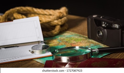 Preparing for an adventure trip. At night, inspection of an old map with a compass and a magnifier under the light of a lamp. Dark background.
