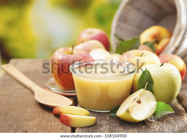 Preparing apple puree or sauce in a small glass\
jar with sliced apple pieces and a wooden spoon on an old wooden\
table outdoors