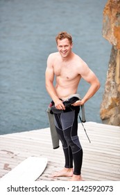 Preparing For An Awesome Day. Young Man Putting On His Wetsuit Before Engaging In Some Watersports.