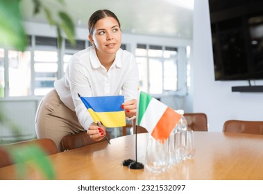 Preparing for business negotiations - woman sets small flags of countries of Ukrain and Italy on the table - Powered by Shutterstock