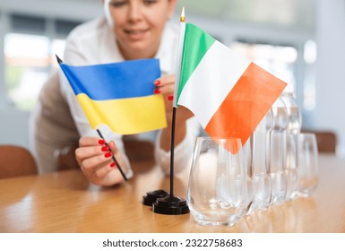 Preparing for business negotiations - woman sets small flags of countries of Ukrain and Italy on the table - Powered by Shutterstock