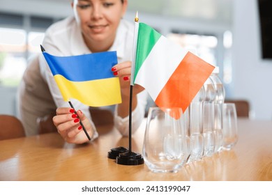 Preparing for business negotiations - woman sets small flags of countries of Ukrain and Italy on the table - Powered by Shutterstock