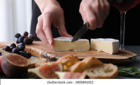 Preparing cheese plate with soft camembert cheese, figs and grapes. Woman's hands slicing cheese