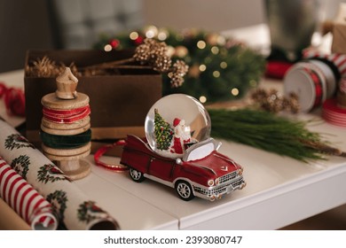 Preparing for Christmas holidays. Beautiful decoration on white table. Wreath and fit tree. Different ribbons and packing papers. Snow globe with Santa  - Powered by Shutterstock