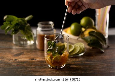 preparing a cocktail by stirring with a spoon a muddled bottom with limes, boil a good bottle of rum liqueur, tequila mojito glass