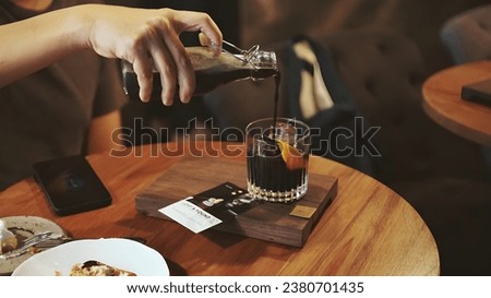 Preparing cold brew coffee with orange juice. A hand pouring cold brew coffee from a bottle can into a highball glass filled. Orange spiced cold brew coffee. Selective focus.