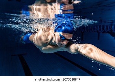 Preparing to competition. Professional male swimmer in swimming cap and goggles in motion and action during training at pool, indoors. Healthy lifestyle, power, energy, sports movement concept