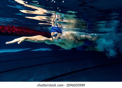 Preparing to competition. Professional male swimmer in swimming cap and goggles in motion and action during training at pool, indoors. Healthy lifestyle, power, energy, sports movement concept - Powered by Shutterstock