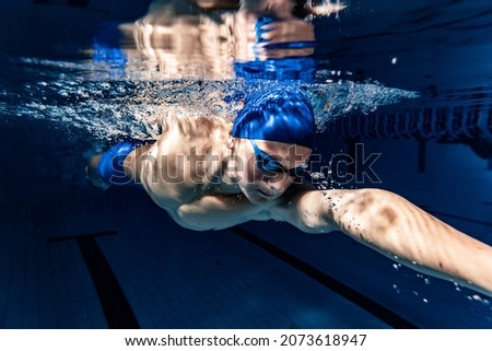 Preparing to competition. Professional male swimmer in swimming cap and goggles in motion and action during training at pool, indoors. Healthy lifestyle, power, energy, sports movement concept