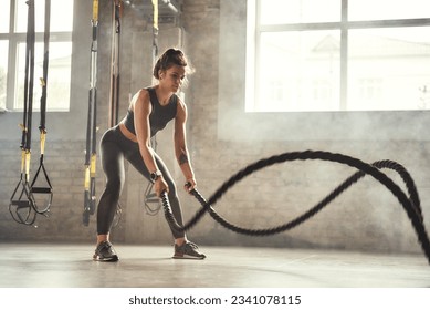 Preparing for the competition. Young athletic woman with perfect body doing crossfit exercises with a rope in the gym. - Powered by Shutterstock