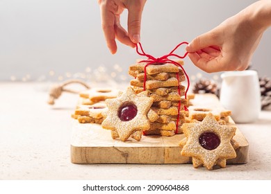 Preparing a cookie gift. Girls hands tying a cotton bow cord. Homemade star or flower shaped linzer cookies with raspberry jam, tied with red ribbon. Christmas or mother day present concept. Selective