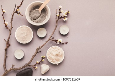 Preparing cosmetic black mud mask on gray background with tender flower. Natural cosmetics for home or salon spa treatment, top view, copy space