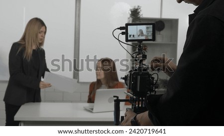 Preparing the crew for the video shoot in the studio. A cameraman sets up a video camera, a female director discusses storyboards and script with the presenter.