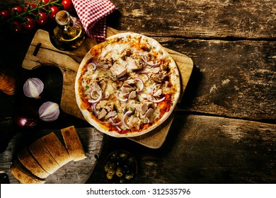 Preparing Delicious Homemade Tuna Pizza In A Rustic Kitchen On An Old Wooden Counter Served With Fresh Bread And Condiments, Overhead View With Copyspace