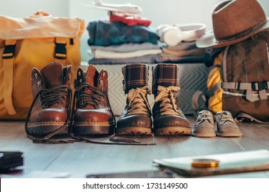 Preparing for a family travel. Father's, mother's and kids hiking shoes standing in a row near backpacks and things indoor. Selective focus on the boots.