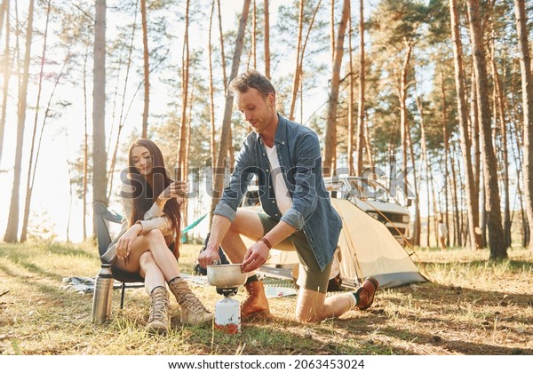 Preparing food. Young couple is traveling in\
the forest at daytime\
together.