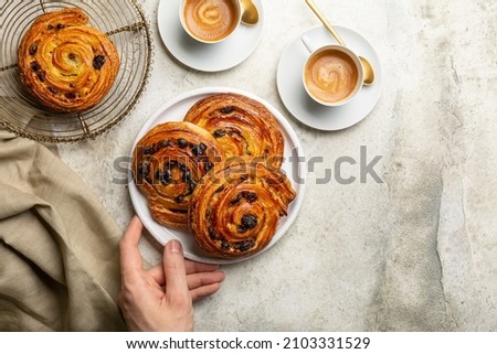 Preparing french or continental breakfast with espresso coffee and croissant. Pain aux raisins, also called escargot or pain russe, is a spiral pastry with custard cream and raisin.