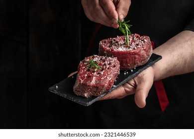 Preparing fresh beef or pork on a dark background. Chef salts steak in a freeze motion with rosemary and spices. Long banner format - Powered by Shutterstock