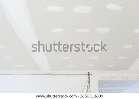 Preparing gypsum board ceiling inside residential building during interior renovation showing electrical wire along smooth edges plastering work underway