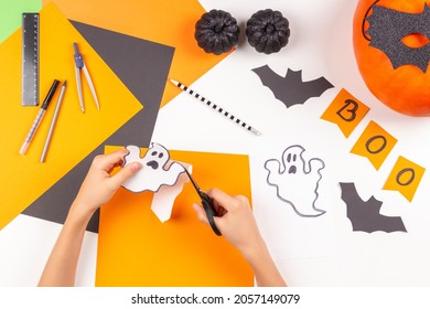 Preparing For Halloween. Teenage Kid Hands Cutting Colored Paper With Scissors And Making Halloween Decorations Over White Desk. Top View.