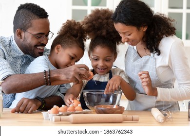 Preparing Home Bakery. Loving Friendly Afro American Family Spouses With Two Diverse Children Elder Daughter And Younger Son Cooking Food Together At Kitchen Table, Mixing Dough For Homemade Pastries