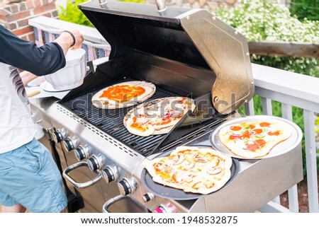 Preparing individual grilled pizzas on an outdoor gas grill.
