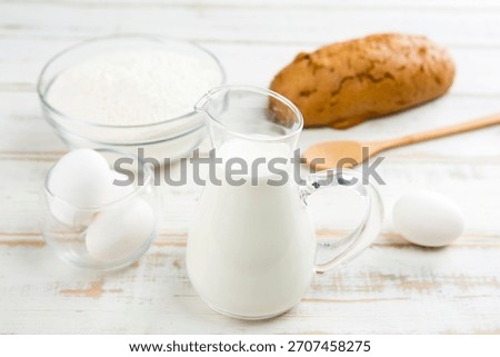 Preparing ingredients for baking bread with milk, flour, eggs, and a loaf of bread on a rustic kitchen table
