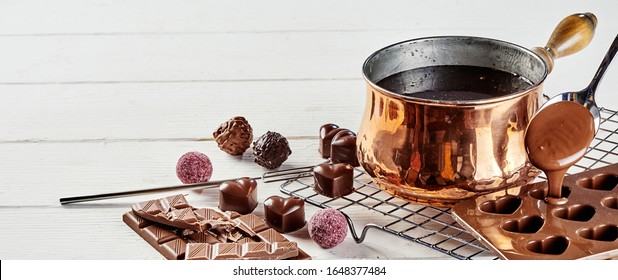Preparing luxury hand made Valentines chocolates pouring melted chocolate from a copper pot into a mould with assorted bonbons on a wire rack - Powered by Shutterstock