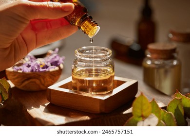 Preparing massage oil dropping essential oil. Woman dripping aromatic essential oil for a spa beauty treatment into a bigger jar. Organic oil for aromatherapy being prepared with herbs and flowers.