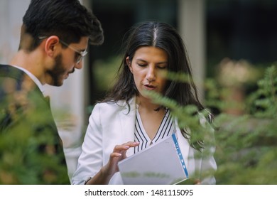 Preparing For Meeting. Two Young Business People Walking Outside On The City Street Reading Through Documents And Talking