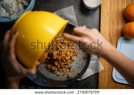 Preparing orange cheesecake by adding crushed biscuit base to a springform pan lined with parchment paper, baking dessert