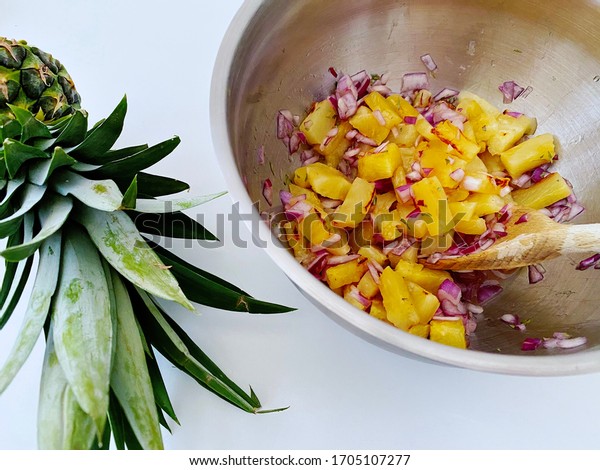 Preparing pineapple dish in kitchen. Ingredients\
for homemade pineapple salsa. Chargrilled chunks with red onion,\
lime juice & coriander in mixing bowl. Sweet twist on classic\
recipe. Fresh home\
food.
