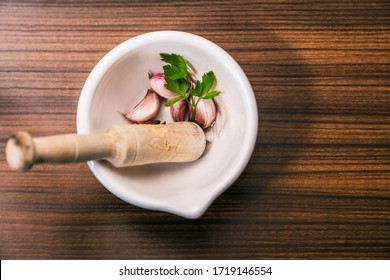 Preparing a recipe to make aioli in a traditional and homemade way. Ingredients and utensils to prepare garlic oil. Different garlic cloves, parsley leaves and a mortar on top of a wooden worktop. - Powered by Shutterstock