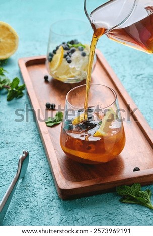 Preparing refreshing drink, iced tea with lemon slices, mint and blueberries in glasses on turquoise concrete background. Soft drinks. Summer drinks