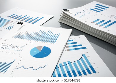 Preparing report. Blue graphs and charts. Business reports and pile of documents on gray reflection background.
