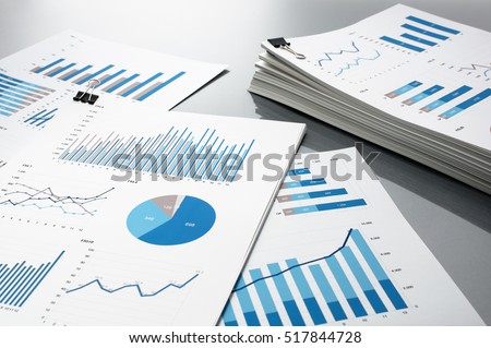 Preparing report. Blue graphs and charts. Business reports and pile of documents on gray reflection background.
