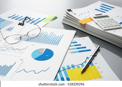 Preparing Report. Blue Graphs, Glasses, Calculator And Pen. Business Reports And Pile Of Documents On Gray Reflection Background.
