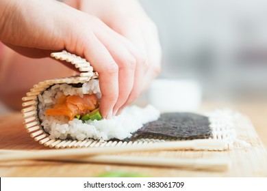 Preparing, rolling sushi. Salmon, avocado, rice on seaweed and chopsticks on wooden table.