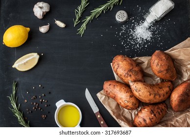 Preparing rosemary roasted sweet potatoes with olive oil, lemon, salt, pepper and garlic - kitchen scenery from above. Black chalkboard as background. Layout with free text space. - Powered by Shutterstock