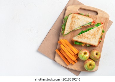 Preparing a school breakfast. Sandwich, carrots and apples on a cutting board on a gray background. Top view, panorama.