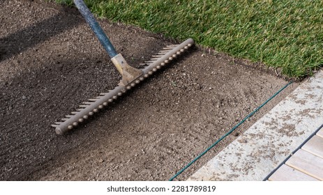 Preparing the soil with a rake for new turf and laying a cable for an automatic lawn mower robot near the terrace - Shutterstock ID 2281789819