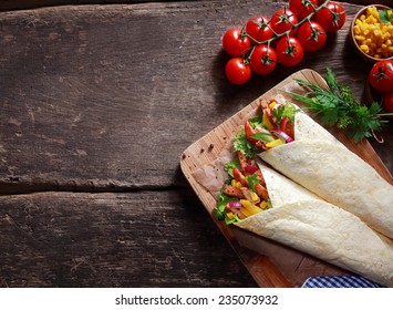 Preparing tasty Tex-Mex tortilla wraps in a rustic kitchen filled with fresh salad ingredients, corn kernels, herbs and diced meat , overhead view with ingredients and copyspace