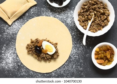 Preparing Traditional Chilean Empanada De Pino, Stuffed With Ground Beef, Onion, Black Olive, Raisin, Hard-boiled Egg, Ingredients On The Side, Photographed Overhead On Slate With Natural Light