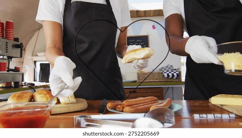Preparing two servers assembling buns and dogs at counter, in white shirts and aprons, heart frame. Marketstall, streetfood, vendor, sausages, cheese, condiments, cuttingboard
