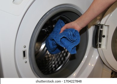 Preparing the wash cycle. Washing machine, hands and clothes. Woman hands loading towel into washing machine. Woman taking blue towel from washing machine.