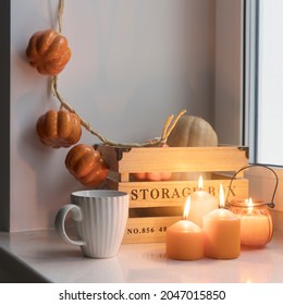 Préparer votre maison pour Halloween. Une citrouille en bois, une guirlande imitant la citrouille, des bougies oranges, une tasse de thé et une lanterne à bougies ornent la fenêtre.