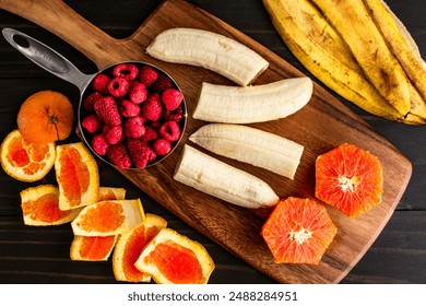 Prepping Fresh Fruit to Make a Smoothie Bowl: Raspberries with peeled and halved bananas and cara cara orange on a wooden cutting board - Powered by Shutterstock