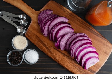 Prepping Ingredients for Pickled Onions: Sliced red onion on a wooden cutting board with kosher sale, black peppercorns, sugar, and bottles of vinegar - Powered by Shutterstock