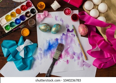 Preprimary painting of Easter Eggs, Brushes, Paints, Eggs, Sweets, Ribbons on the Dark Wooden Table. The concept of Easter. Flat lay, top view.