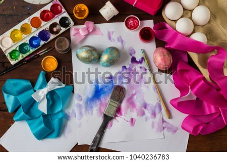 Preprimary painting of Easter Eggs, Brushes, Paints, Eggs, Sweets, Ribbons on the Dark Wooden Table. The concept of Easter. Flat lay, top view.